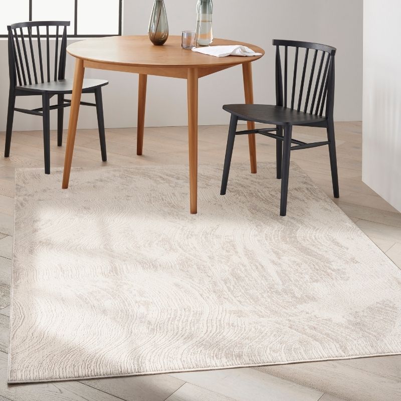 A large off-white area rug with a subtle wavy pattern, shown in a dining room setting under a round wooden table and two black chairs.