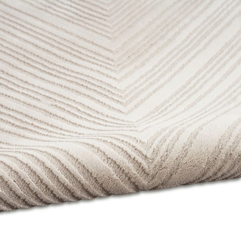 A close-up of a textured area rug with a chevron pattern in warm off-white and beige tones, showing the detailed loop pile texture and folded corner.