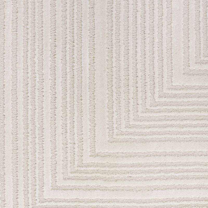 A close-up of a textured area rug featuring a modern chevron or stepped geometric pattern in warm off-white and light beige tones.
