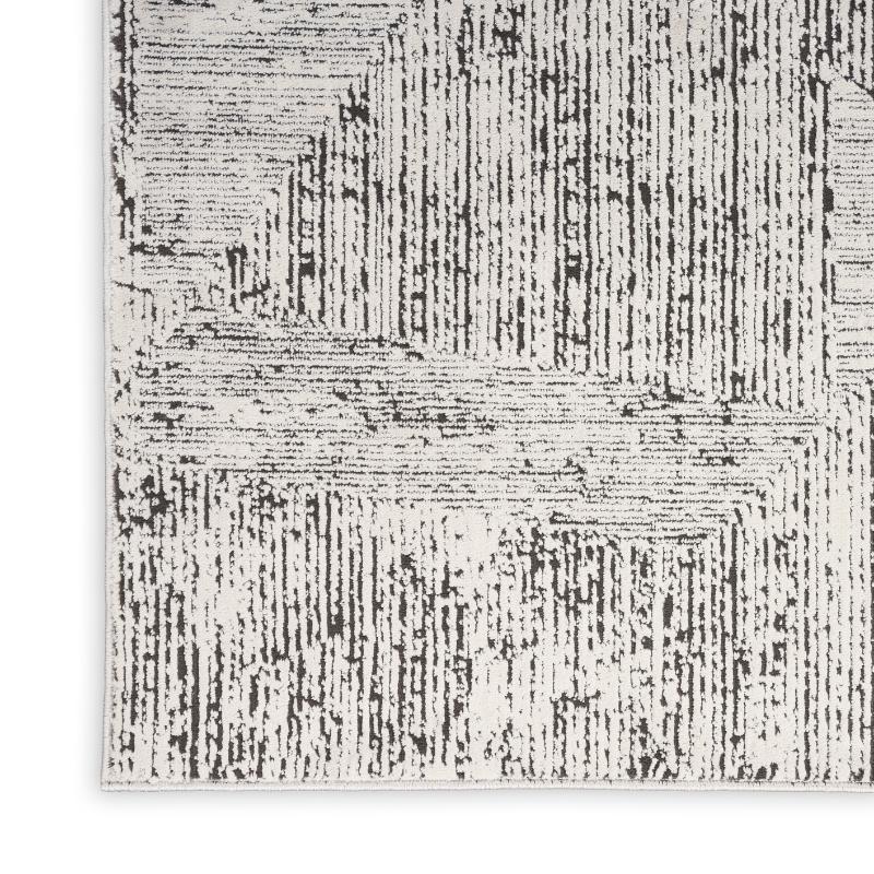 A close-up of a textured area rug featuring a distressed, vertical brushstroke pattern in black and off-white.