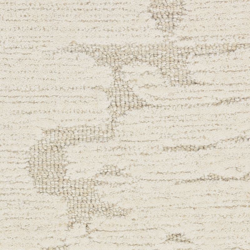 A close-up of a textured area rug with an abstract, distressed pattern in cream and light taupe.