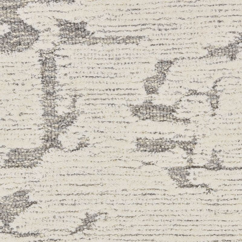A close-up of a textured area rug with a distressed, abstract pattern in charcoal gray on an off-white background.