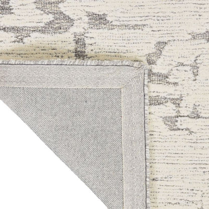Close-up of a rug corner showing the cream and gray distressed pattern on top and the light gray underside with fringed edge.