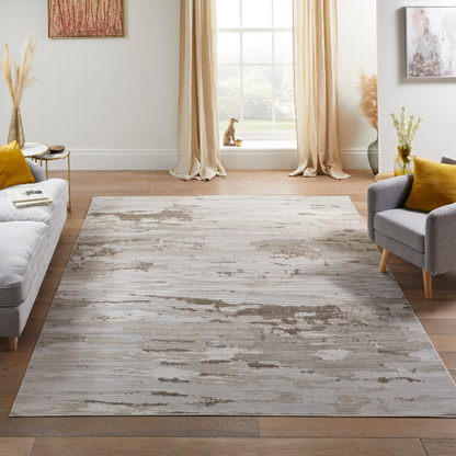 A rectangular area rug with a distressed, weathered wood-look pattern in shades of gray and beige, shown in a modern living room setting with a gray sofa, armchair, and wooden floor.