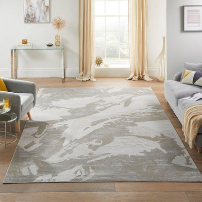 A large rectangular area rug with an abstract gray and off-white pattern, styled in a bright, modern living room with a gray sofa, armchair, and wooden floor.