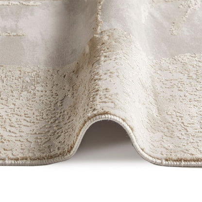 A close-up of a textured area rug in a warm cream or off-white tone, showing the pile texture and rolled corner detail against a white background.
