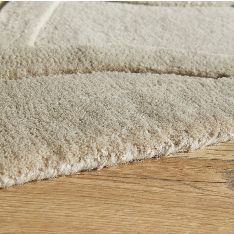 Close-up of a plush, textured area rug in a warm cream or off-white color, shown folded over to display its pile and edge, resting on a light brown wooden floor.