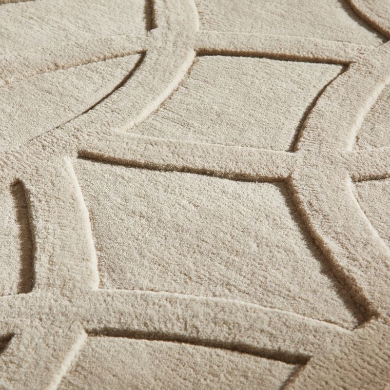 Close-up of a textured area rug with a geometric lattice pattern in a warm cream or beige tone.