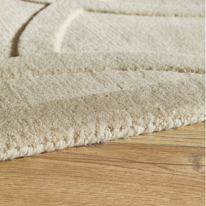 Close-up of a cream-colored textured rug with a raised geometric pattern, shown on a light brown wooden floor.