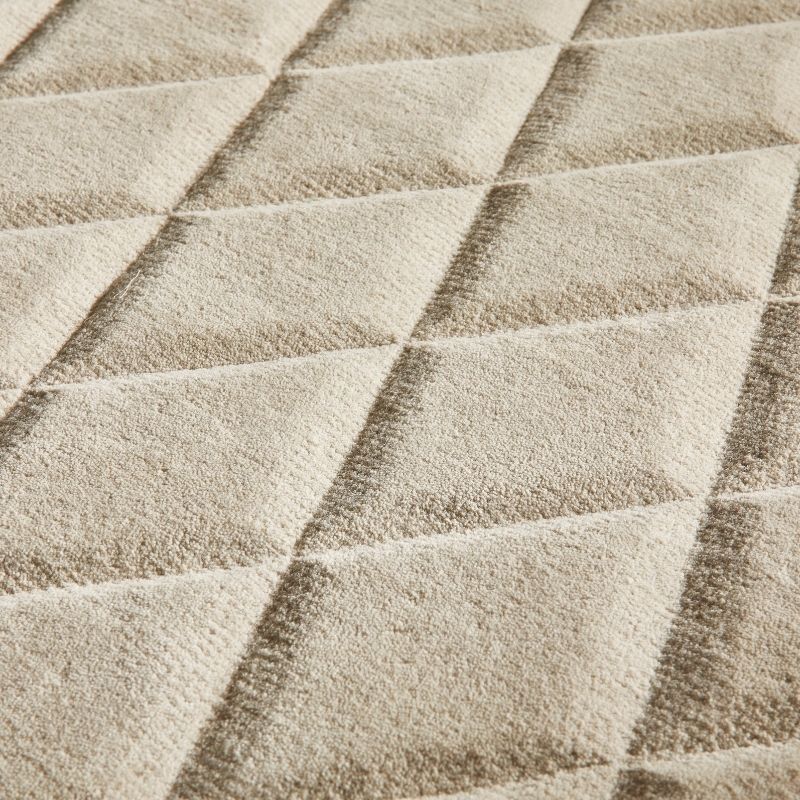 Close-up of a textured fabric surface with a repeating diamond quilted pattern in warm beige and cream tones.