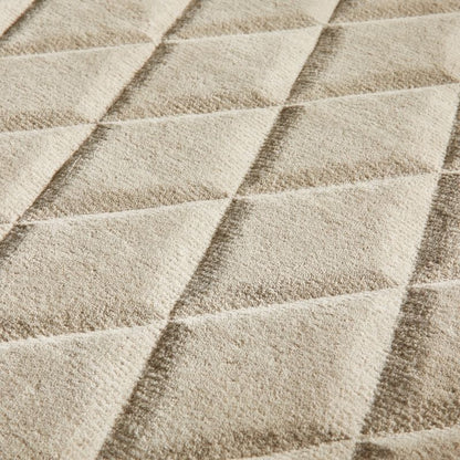 Close-up of a textured fabric surface with a repeating diamond quilted pattern in warm beige and cream tones.