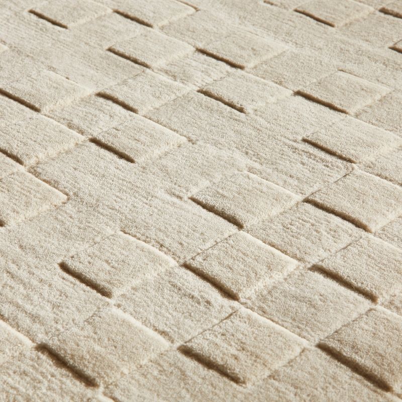 A close-up of a textured area rug with a woven herringbone pattern in a warm cream or off-white color.