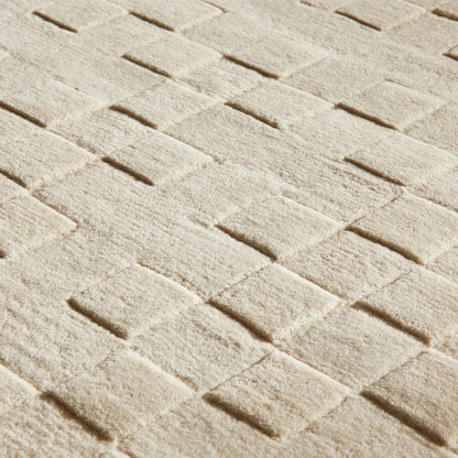 A close-up of a textured area rug with a woven herringbone pattern in a warm cream or off-white color.