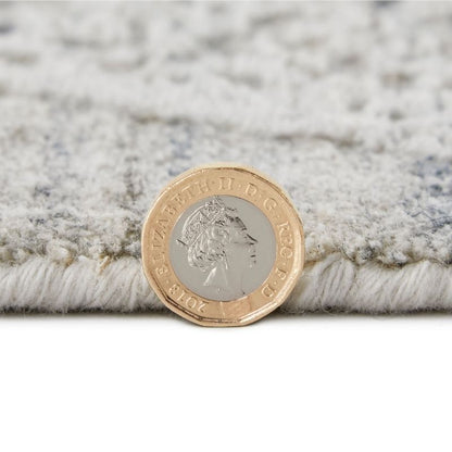 A close-up of a plush, textured area rug in a light gray and white pattern, with a British two-pound coin placed on top to show scale.