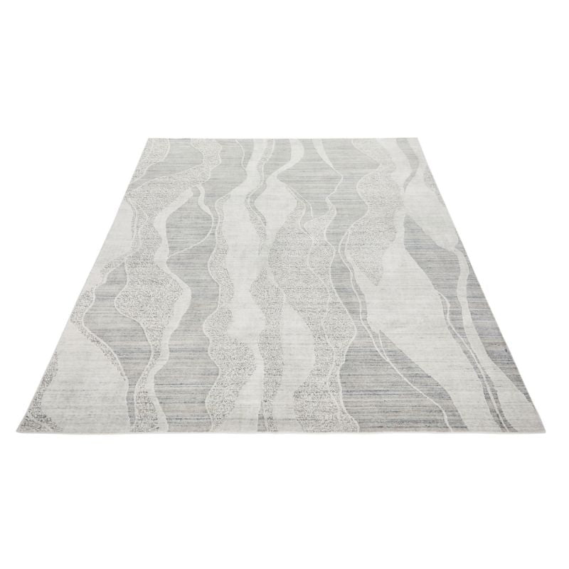 A rectangular area rug with a modern abstract pattern of wavy vertical lines in shades of gray, white, and light taupe, shown from an elevated perspective against a plain white background.
