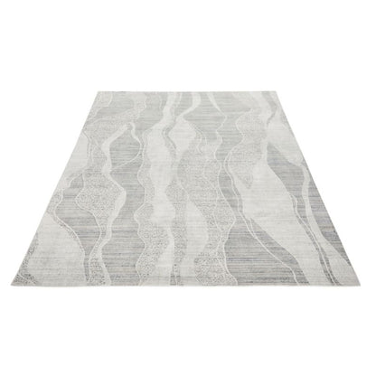 A rectangular area rug with a modern abstract pattern of wavy vertical lines in shades of gray, white, and light taupe, shown from an elevated perspective against a plain white background.