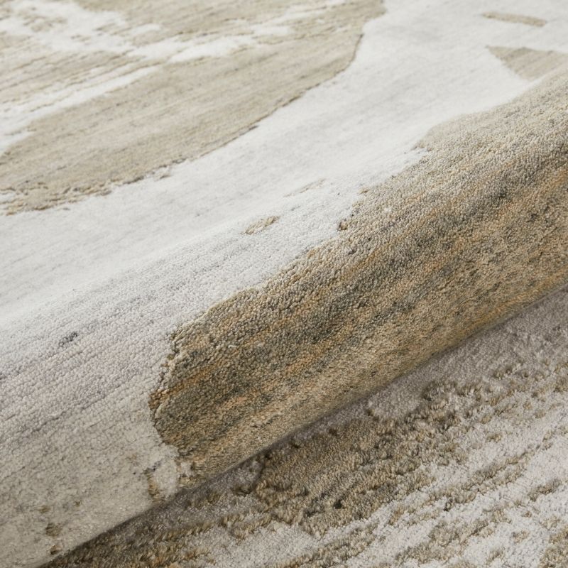 Close-up of a textured area rug with an abstract pattern in shades of beige, cream, and gray, showing the pile and weave detail.