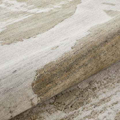 Close-up of a textured area rug with an abstract pattern in shades of beige, cream, and gray, showing the pile and weave detail.