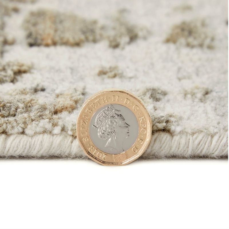 A close-up of a textured area rug in cream and beige tones, shown with a British two-penny coin placed on top for scale.