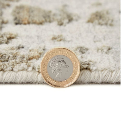 A close-up of a textured area rug in cream and beige tones, shown with a British two-penny coin placed on top for scale.