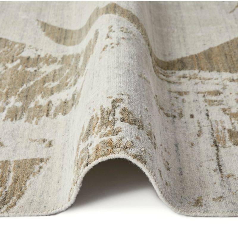 A close-up of a textured area rug with a distressed abstract pattern in beige and off-white, shown draped to display its pile and edge.