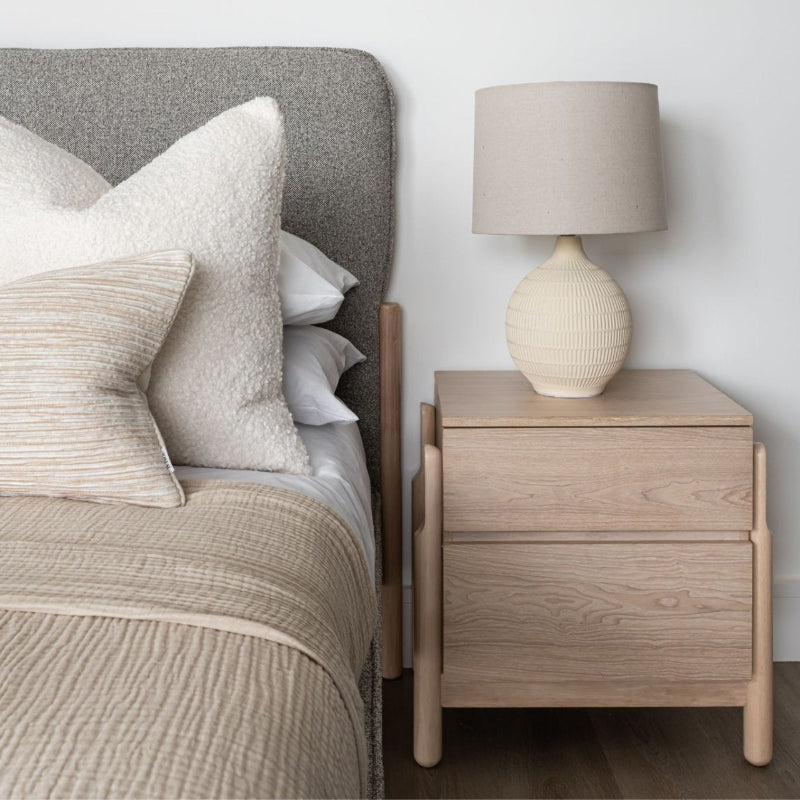 Bedroom setting with a bed and wooden nightstand featuring a lamp.