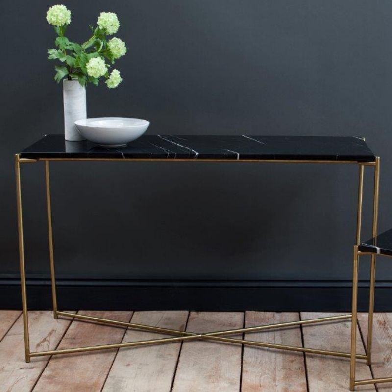 Console table with black marble top and gold legs against a dark wall.